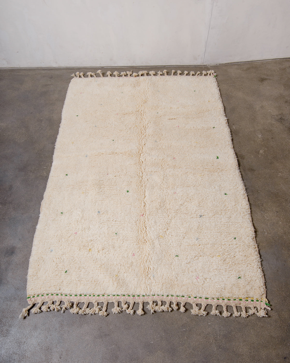 Berberlin Beniourain rug in cream wool with coloured dots laying on concrete floor.